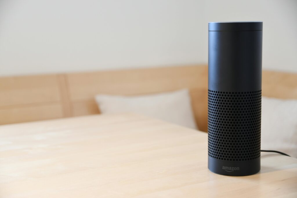 pexels-photo-977296-977296 A black smart speaker resting on a light-colored wooden table in a cozy indoor setting.